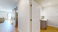 This thoughtfully laid-out single-floor residence offers a seamless blend of modern design and functional living across its one-bedroom, one-bathroom floor plan. Light wood flooring flows consistently throughout, tying each space together with a warm, cohesive feel.

The kitchen is a standout feature, showcasing white shaker-style cabinetry extending to the ceiling, stainless steel appliances, a matte black faucet over a white countertop sink, and a peninsula with seating — ideal for casual dining. Natural light pours in through a large sliding glass door at the end of the open living area, which accommodates comfortable lounge seating beneath a trio of framed nature-inspired artwork.

The hallway connecting the rooms features a stylish sliding barn door with black hardware, adding a contemporary touch. The bedroom offers a calm, restful atmosphere with soft neutral walls, recessed lighting, and ample room for a full furniture arrangement. The bathroom includes a full tub-shower combo with clean white tile surround, wood-look flooring, and a vanity with light countertops and taupe cabinetry. Every detail reflects a clean, modern aesthetic designed for comfortable everyday living.
