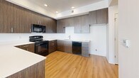 Located in Ogden, Utah, this well-appointed 3-bedroom, 2-bathroom unit offers a thoughtfully designed single-floor layout with modern finishes throughout. The open-concept kitchen and living area serves as the heart of the home, featuring rich dark wood cabinetry, white countertops, black appliances including a range, microwave, and dishwasher, and light wood-style flooring that flows seamlessly through the main living spaces. A breakfast bar peninsula adds additional prep and dining space. The living area is bright and airy, bathed in natural light from large windows and a glass door that opens to a private balcony, offering outdoor views of the surrounding area. A central hallway connects the three bedrooms, each carpeted and filled with natural light from generously sized windows. The spacious primary bedroom provides a comfortable retreat. Both bathrooms are finished with dark wood vanities, white countertops, and light flooring; one features a tub-shower combination. Additional highlights include five closets for ample storage, an in-unit laundry room, and recessed lighting throughout. The clean, contemporary aesthetic and functional layout make this a practical and attractive living space.