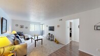 This single-floor unit offers a well-organized layout designed for comfortable everyday living. The living room serves as the central gathering space, finished with plush wall-to-wall carpeting and a textured ceiling. A large sliding glass door leads to a private balcony, filling the room with natural light and providing pleasant outdoor views. The open feel of the space is enhanced by clean white walls and a seamless transition to wood-style flooring in the entryway and adjoining areas.

The galley-style kitchen is efficiently arranged with dark wood cabinetry lining both sides, offering generous storage and counter space. White appliances, including a refrigerator and electric range, complement the light countertops, while wood-style flooring ties the space together practically.

The primary bedroom is generously proportioned, featuring soft carpeting and a walk-in closet with built-in shelving. A second bedroom, also carpeted, provides a comfortable and versatile space suitable for various uses. The full bathroom includes a combined tub and shower, a single vanity with wood cabinetry, and wood-style flooring, presenting a clean and functional design throughout.