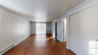 Located at 8 Osterville in Yarmouth, Maine, this single-floor unit offers a clean, functional layout with consistent design details throughout. Rich hardwood flooring runs throughout the living spaces, adding warmth and a polished feel to every room.

The main living area is generously sized, featuring a large sliding glass door dressed with vertical blinds that fills the space with natural light and offers views of the surrounding wooded landscape. A textured popcorn ceiling and soft gray walls create a neutral backdrop, while baseboard heating ensures year-round comfort.

The kitchen is well-appointed with warm-toned wood cabinetry, stone-look laminate countertops, a stainless steel sink positioned beneath a bright window, and white appliances including a dishwasher. The layout provides ample counter and storage space for everyday cooking needs.

The bedroom is spacious and bright, benefiting from two windows that allow abundant natural light to pour in. A full-width double bi-fold closet offers generous storage, and the same rich hardwood flooring continues throughout.

The bathroom features a clean, all-white tub and shower surround with chrome fixtures, offering a simple and functional design. Overall, this unit presents a tidy, move-in ready space with practical features throughout.