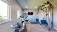 Located at 218 19th St SE in Watertown, South Dakota, this dedicated exercise room offers a practical and well-organized fitness environment. The single-room space is finished with durable carpet tile flooring and painted in a cool, neutral gray-blue tone that creates a calm, focused atmosphere conducive to working out.

The room is equipped with a range of fitness equipment to support varied workout routines. A multi-station cable machine serves as the centerpiece, providing options for strength training and resistance exercises. Stationary bikes offer cardiovascular training, while a dumbbell rack, adjustable weight bench, stability ball, and exercise mat round out the functional setup. A wall-mounted flat-screen television adds entertainment value during workouts.

Natural light enters through multiple windows positioned along the walls, brightening the interior and offering views of the surrounding outdoor environment. Recessed ceiling lighting supplements the natural light, ensuring the space remains well-lit at all times. A wall-mounted HVAC unit provides climate control for year-round comfort.

The layout makes efficient use of the available floor area, with clearly defined zones for cardio, strength training, and floor exercises. A standard entry door with a keypad lock provides secure access. Overall, the space delivers a clean, functional fitness facility suited for regular personal or shared use.