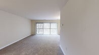 This single-floor, 2-bedroom, 1-bathroom residence offers a thoughtfully arranged layout designed for comfortable everyday living. The spacious living room is a standout feature, showcasing wall-to-wall carpeting and large sliding glass doors fitted with vertical blinds that invite abundant natural light and provide views of the surrounding greenery. The open sightline between the living room and kitchen enhances the sense of space and connectivity.

The kitchen is well-equipped with warm medium-toned wood cabinetry, light granite-style countertops, and black appliances including a gas range, built-in microwave, dishwasher, and stainless steel refrigerator. Light wood-look flooring completes the kitchen's clean, functional aesthetic.

Both bedrooms feature plush wall-to-wall carpeting and large windows with vertical blinds, providing ample natural light. The generously sized primary bedroom includes a walk-in closet with dual hanging rods, offering practical storage. A second closet serves additional storage needs.

The full bathroom is finished with tile flooring, a white vanity with a medicine cabinet mirror, lighted vanity bar, and a tub/shower combination. Throughout the unit, neutral warm-beige walls create a bright and cohesive atmosphere, making the space feel open and move-in ready.