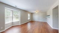 This single-floor, 2-bedroom, 1-bathroom home offers a practical and cohesive layout throughout. Warm-toned hardwood-style flooring extends consistently across every room, creating a unified and inviting atmosphere. The combined kitchen and living area serves as the heart of the home, with the spacious living room featuring multiple windows that invite abundant natural light and views of surrounding greenery. A ceiling fan with a light fixture adds functionality and comfort. A bay-style window arrangement in the living room further enhances the sense of openness. The galley-style kitchen is efficiently designed with white cabinetry, light countertops, a stainless steel sink, and white appliances including a refrigerator and stove, maximizing the available space. Both bedrooms are well-proportioned with neutral gray-toned walls and windows that bring in natural light. The primary bedroom offers a closet with louvered bi-fold doors and built-in shelving and hanging rods. The second bedroom also includes a window with outdoor views. The full bathroom features a tub-shower combination, a toilet, a vanity with a warm wood cabinet, and light flooring. Two hallways connect the rooms, providing a smooth flow throughout the home.