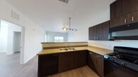 This single-floor residence offers a clean, modern layout with consistent wood-look flooring throughout all living areas. The open-concept kitchen is a central highlight, featuring dark espresso cabinetry with ample upper and lower storage, light-toned countertops, a double-basin sink, a pendant track light fixture, and a full suite of black appliances including a gas range, over-the-range microwave, dishwasher, and refrigerator. The kitchen opens directly to the living area, which benefits from natural light and slider door access to a private balcony with open outdoor views. A dedicated in-unit laundry closet with a stacked washer and dryer is conveniently located just off the kitchen. The bedrooms are bright and well-sized, each featuring wood-look flooring, neutral white walls, and large windows that invite generous natural light and scenic outdoor views. One bedroom includes a built-in closet with a rod and shelf system. Two full bathrooms serve the unit, each finished with dark wood-toned vanity cabinetry, light countertops, a tub/shower combination, and matching wood-look flooring. The overall aesthetic is contemporary and neutral, offering a cohesive, move-in ready environment throughout.