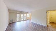 This well-appointed one-bedroom, one-bathroom residence in Pikesville, Maryland offers a thoughtfully laid-out single-floor plan encompassing a comfortable living room, dining room, kitchen, bedroom, bathroom, hallway, and closet. Consistent hardwood-style flooring flows throughout, lending a clean and cohesive aesthetic to the entire space. The living room is generously sized, featuring French doors that fill the room with natural light and provide views of the surrounding greenery. Adjacent to the living area, the dining room is accented by an elegant wrought-iron chandelier and a window that adds additional brightness. The kitchen is well-equipped with warm wood cabinetry, blue-gray countertops, a double sink, and white appliances including a refrigerator, gas range, microwave, and dishwasher. A convenient in-unit stacked washer and dryer is tucked neatly behind louvered doors within the kitchen area. The spacious primary bedroom features a large window for natural light and direct access to a dedicated closet. The bathroom offers a full tub-shower combination with classic white tile surround. Neutral cream-toned walls throughout create a bright, inviting atmosphere well-suited for comfortable everyday living.