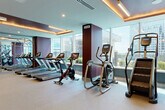 This modern fitness center is thoughtfully designed across a single floor, offering a comprehensive workout experience through several distinct zones. The cardio area is a standout, lined with floor-to-ceiling windows that flood the space with natural light and frame sweeping city skyline views. Treadmills, stationary bikes, elliptical trainers, and a stair climber are arranged to take full advantage of the scenery, complemented by a coffered ceiling with warm ambient lighting strips.

The strength training area features a rich color palette of deep plum, burgundy, and teal walls, creating an energizing atmosphere. It is outfitted with Matrix cable machines, free weights, barbells, weight racks, and adjustable benches, all set on neutral carpet flooring beneath a geometrically recessed ceiling with warm uplighting. A wall-mounted television adds a functional entertainment element.

The entryway makes a striking first impression with bold, large-scale abstract graphic murals covering the walls, lending a contemporary and artistic character to the arrival experience. A water station is conveniently positioned near the entrance.

A dedicated yoga and stretching studio rounds out the facility, featuring a vibrant graffiti-style mural wall, cork flooring for comfort, and a clean, open layout ideal for mat-based workouts and mindful movement.