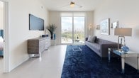 This contemporary residence offers a well-designed open-concept layout spread across a single floor, delivering a bright and cohesive living experience throughout. The living room is a standout space, featuring large sliding glass doors that lead to a private balcony with sweeping city skyline views. Light tile flooring, a ceiling fan, and clean white walls create a modern, airy atmosphere in this central gathering area.

The galley-style kitchen is efficiently arranged with dark cabinetry, white countertops, and stainless steel appliances, including a range and dishwasher, offering a functional and stylish cooking environment.

Adjacent to the kitchen, the dining area provides an elegant setting highlighted by soaring ceilings and large framed artwork, lending the space a refined character.

The residence includes multiple bedrooms, each benefiting from generous natural light through large windows that frame city views. The bedrooms feature light-toned flooring and ample closet space, including built-in shelving systems. Two bathrooms are finished with striking marble-look porcelain tile flooring; one includes a glass-enclosed walk-in shower, while the other offers a vanity with dark cabinetry. Together, these spaces reflect a consistent modern aesthetic, making this residence a polished and comfortable urban retreat.