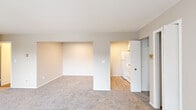 This 2-bedroom, 1-bathroom single-floor unit offers a straightforward and functional layout across a comfortable footprint. The living room is the largest area of the home, featuring neutral-toned carpet, a bank of large windows with vertical blinds that allow abundant natural light, and a wall-mounted air conditioning unit. Baseboard heating runs throughout the unit, providing consistent warmth. The kitchen is efficiently designed with light wood-look flooring, white cabinetry, a white refrigerator, and an electric range, offering all essential appliances in a compact space. Both bedrooms are carpeted and well-lit, each featuring vertical blinds over windows that frame outdoor views. The primary bedroom includes a built-in closet with bifold doors, offering organized storage space. The bathroom presents a clean, white aesthetic with wood-look flooring, a single vanity with cabinet storage, a mirrored medicine cabinet with overhead lighting, and a full bathtub with a shower. A hallway connects the rooms in an efficient flow throughout the unit. With neutral warm-beige walls and consistent finishes, this unit presents a clean, move-in ready environment well-suited for practical, comfortable living.