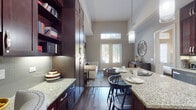 This single-floor residence showcases a thoughtfully designed open-concept layout that seamlessly connects the kitchen, dining, and living areas. Soaring ceilings amplify the sense of space throughout, while large French doors and transom windows flood the interior with abundant natural light and provide views of the outdoors.

The kitchen is a standout feature, outfitted with floor-to-ceiling rich dark espresso cabinetry, light granite countertops, a tile backsplash, and a full suite of stainless steel appliances. A generous kitchen island with bar seating serves as both a functional workspace and an informal dining area, illuminated by contemporary pendant lighting. Built-in open shelving adds additional storage and display space.

The living area offers a welcoming atmosphere with warm-toned walls, hardwood-style flooring, and ample room for comfortable furnishings. A dedicated bedroom features plush carpeting, elevated ceilings, and large windows that invite natural light. The bathroom is finished with matching dark cabinetry, granite countertops, large-format tile flooring, and a soaking tub with tiled surround, maintaining a consistent, polished aesthetic throughout the residence.
