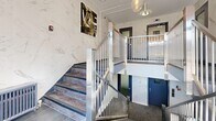 Located at 550 Eglinton Ave W in Toronto, this two-floor common area serves as the building's primary entry and circulation space. The design is anchored by striking marble-effect wall cladding in white and grey tones, which carries consistently across both levels to create a polished, cohesive aesthetic.

The ground floor functions as the main entry lobby, featuring large floor-to-ceiling windows that flood the space with natural light and provide an open view to the streetscape. A pendant chandelier with globe bulbs adds a refined decorative touch above the staircase landing. Large-format dark porcelain floor tiles provide a durable and contemporary contrast to the light wall surfaces.

A sleek stainless steel staircase with vertical metal balusters connects the two floors, offering both a functional and visually prominent architectural element. The upper floor houses an elevator with brushed stainless steel doors, flanked by navy blue-framed doors leading to additional building areas. Subtle artwork is displayed on the upper landing walls, adding character to the transitional space.

The overall ambiance is clean, bright, and modern, with a strong emphasis on durable premium finishes. Security features, including cameras and intercom panels, are discreetly integrated throughout both levels, reflecting a well-considered functional design suited to a contemporary residential or mixed-use building.