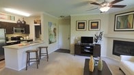 Located at 1250 S. Dayton Ct in Denver, Colorado, this single-story residence offers a thoughtfully designed open-concept layout that maximizes both functionality and comfort. The living area serves as the heart of the home, featuring plush neutral carpeting, crown molding, and a ceiling fan that adds both style and practicality. Warm, neutral-toned walls create an inviting ambiance, while framed wall art adds a personalized touch to the space.

The kitchen flows seamlessly into the living area by way of a breakfast bar with barstool seating — an ideal setup for casual dining or entertaining. The kitchen is equipped with a sink and countertop workspace visible from the main living area, reinforcing the open and connected feel of the floor plan.

The front entry, finished with a classic white door and tile flooring, transitions smoothly into the carpeted living space, creating a natural delineation between zones. A media console along the main wall of the living room provides practical storage and a dedicated area for entertainment.

Overall, the space presents a clean, cohesive aesthetic with functional design choices, making it a welcoming and well-appointed residence in the Denver area.