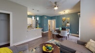 Located at 4800 Waterford Point Dr in Raleigh, NC, this single-floor residence offers a thoughtfully designed open-concept layout that seamlessly connects the kitchen, dining, and living areas. The interior is distinguished by bold teal accent walls, warm wood-style flooring, and textured ceilings that add depth and character throughout.

The living room is a welcoming and comfortable space, featuring a ceiling fan, large windows with blinds and floor-length drape panels that invite natural light, and ample room for generous seating arrangements. Adjacent to the living area, the dining space accommodates a full dining set and flows effortlessly into the kitchen.

The kitchen is well-appointed with white cabinetry, granite-look countertops, a breakfast bar peninsula with pendant lighting, and a full suite of stainless steel appliances including a refrigerator, range, microwave, and dishwasher. The galley-style layout maximizes functionality and storage.

The bathroom showcases grey cabinetry with brushed nickel hardware, granite-look countertops, a large vanity mirror, and a shower/tub combination. Wood-style flooring and a textured ceiling continue the cohesive design language found throughout the home. Track and ceiling fan lighting fixtures provide both style and practicality across all areas of this well-finished residence.
