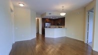This single-floor residence offers a thoughtfully designed open-concept layout that effortlessly connects the living and kitchen areas, creating a spacious and inviting atmosphere. Rich hardwood flooring flows throughout, adding warmth and a sense of continuity across the space.

The kitchen is a standout feature, showcasing dark espresso cabinetry that provides generous storage and a striking visual contrast against the light-toned walls. Stainless steel appliances, including a refrigerator and microwave, lend a modern, polished finish. A peninsula with a light-colored countertop extends from the kitchen, offering additional workspace and a natural gathering point that opens to the living area.

A pendant light fixture hangs elegantly above the peninsula, providing focused task lighting while also serving as a decorative accent. Recessed lighting in the kitchen ceiling ensures the workspace remains bright and functional.

The open living area benefits from the clean sightlines created by the layout, making the space feel expansive and airy. Light, neutral-toned walls throughout enhance the brightness of the interior. A hallway visible from the main living area leads to additional rooms, suggesting a practical and well-organized floor plan. Overall, the space strikes a balance between modern aesthetics and functional everyday living.