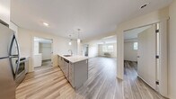 Located at 1465 KLO Road in Kelowna, BC, this well-appointed 2-bedroom, 2-bathroom unit offers a thoughtfully designed single-floor layout. The open-concept kitchen and living area serves as the heart of the home, featuring a large island with a white quartz countertop, modern pendant lighting, grey cabinetry, a grey subway tile backsplash, and stainless steel appliances including a refrigerator, stove, and microwave. Light hardwood-style flooring runs continuously throughout, lending a cohesive and contemporary feel to the entire space. The living area is bright and airy, benefiting from natural light through windows that frame outdoor greenery. Both bedrooms are comfortably sized, each featuring ceiling fixtures and windows that allow in natural light, with the primary bedroom offering generous proportions. The two bathrooms are finished in a clean, modern style with grey cabinetry, white quartz countertops, tile backsplashes, and tub-shower combinations. A dedicated laundry room houses a full-sized washer and dryer alongside additional shelving for storage. A walk-in closet provides further organizational space. Neutral tones and consistent finishes throughout create a calm, move-in-ready atmosphere ideal for comfortable everyday living.