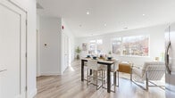 Located at 15 Washington Ave in Suffern, NY, this thoughtfully designed one-bedroom, two-bathroom residence offers a bright and contemporary living experience on a single floor. The open-concept kitchen and living area serves as the heart of the home, featuring light hardwood flooring, recessed lighting, and a bank of large windows that frame scenic views of the surrounding neighborhood and hillside. The kitchen is appointed with sleek, high-gloss gray cabinetry, white quartz countertops, a subway tile backsplash, and a full suite of stainless steel appliances. The living and dining areas flow seamlessly, creating a versatile and welcoming space filled with natural light. The spacious primary bedroom offers a serene retreat with continued hardwood flooring and generous proportions. The two bathrooms are elegantly finished — one showcasing a deep soaking tub set against dramatic full-height marble-effect tile walls, while the other features classic white cabinetry and tile flooring. A dedicated closet provides practical storage. Throughout, the residence maintains a clean, modern aesthetic defined by a crisp white palette, quality materials, and an abundance of light from multiple oversized windows.