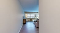 Located at 500 Fulton St E in the heart of Grand Rapids, Michigan, this 2-bedroom, 1-bathroom residence offers a practical and comfortable single-floor layout. The living room serves as the centerpiece of the home, featuring durable hardwood-style flooring, neutral-toned walls, and multiple windows that invite generous natural light. The open feel of the space is enhanced by clean lines and a straightforward design.

The galley-style kitchen is efficiently arranged with white cabinetry, dark countertops, a black refrigerator, and an electric range, complemented by open shelving that adds storage flexibility. A hallway connects the main living areas to the private quarters.

The spacious primary bedroom is notably generous in size, featuring plush carpeting, dual windows overlooking the outdoors, and ample room for a full furniture arrangement including a desk workspace. The second bedroom is equally well-appointed with carpet flooring, a closet with louvered doors, and a window for natural light.

The bathroom features classic light-blue subway tile wainscoting, a wall-mounted sink, a mirrored medicine cabinet, and a shower-tub combination. Throughout the residence, the consistent use of neutral tones and hardwood-style flooring in the main areas creates a cohesive, understated aesthetic well-suited for everyday living.