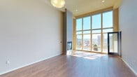 Located on the 8th floor at 1142 Fawcett Ave in downtown Tacoma, this single-level unit offers a striking combination of contemporary design and urban convenience. The expansive living area immediately commands attention with its soaring ceilings, rich hardwood flooring, and a dramatic wall of floor-to-ceiling windows that frame sweeping views of the Tacoma skyline and beyond. A sleek, modern fireplace anchors the living space, adding warmth and architectural interest. The open-concept layout connects the living area seamlessly to the kitchen, which is outfitted with warm wood cabinetry, dark granite countertops, stainless steel appliances including a gas range, dishwasher, and French door refrigerator, and a large central island with pendant lighting overhead — ideal for both cooking and entertaining. The bedroom is generously proportioned with plush carpeting and direct access to a walk-in closet. The primary bathroom features dual sinks with tile surround, a glass-enclosed standing shower, and a soaking tub. A second bathroom includes a full tub/shower combination and rich wood vanity cabinetry. An in-unit washer and dryer add everyday convenience, completing this well-appointed urban residence.