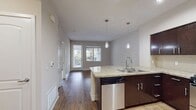 This 580 square foot apartment in Santa Ana, CA offers a thoughtful blend of modern amenities and efficient design. The single-bedroom unit features two full bathrooms, enhancing convenience for residents and guests. The open-concept layout seamlessly integrates the kitchen and living areas, creating a sense of spaciousness.

The kitchen is a standout feature, boasting dark wood cabinetry, granite countertops, and stainless steel appliances. A curved breakfast bar adds functionality and style, perfect for casual dining or entertaining. The living area flows into the kitchen, with warm wood flooring unifying the space.

The bedroom, measuring 150 square feet, offers ample space and is carpeted for comfort. Large windows provide natural light and views of the surrounding area. Storage solutions are plentiful, with built-in shelving and a closet featuring both hanging space and shelves.

Bathrooms are well-appointed with modern fixtures, including a double vanity in one. Tile flooring in the bathrooms contrasts nicely with the wood and carpet used elsewhere. Throughout the apartment, recessed lighting and pendant fixtures provide a warm ambiance.

The neutral color palette and clean lines create a contemporary feel, allowing residents to easily personalize the space. Despite its compact size, this apartment maximizes every square foot, offering a comfortable and stylish living environment.