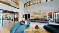 Located at 5745 Golden Triangle Blvd in Fort Worth, Texas, this single-floor community clubhouse delivers a bold and sophisticated interior designed for social gatherings and everyday relaxation. The space greets visitors with soaring double-height ceilings, clerestory windows that flood the main lounge with natural light, and a dynamic mix of geometric patterned tile and light hardwood-style flooring.

The main lounge area centers around a curved teal velvet sofa, a glass-top coffee table, and an eclectic area rug in warm yellows and blues, creating a vibrant yet inviting atmosphere. An entertainment nook features dual wall-mounted flat-screen TVs set against a dramatic dark wood-paneled accent wall, complemented by a bold teal painted wall, a channeled gold booth banquette, and retro-inspired accent chairs with striped upholstery.

The kitchen and bar area is a true standout, boasting an expansive quartz-topped island with geometric-tiled siding, black cabinetry with brass hardware, a luminous glazed tile backsplash, and a striking cascade of gold pendant lights overhead. A full bank of appliances and a black undermount sink make this space highly functional. Glass-partitioned rooms off the main corridor provide flexible private spaces, while curated artwork and sophisticated lighting complete the upscale, modern ambiance throughout.