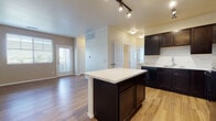 This single-floor residence offers a thoughtfully designed open-concept layout that seamlessly connects the kitchen and living areas. The kitchen is a standout feature, showcasing rich dark-espresso cabinetry that extends to the ceiling, crisp white countertops, a central island with additional storage, and a full suite of black appliances including a range, microwave, dishwasher, and refrigerator. Track lighting and wood-look flooring complete the kitchen's modern aesthetic.

The open living area flows naturally from the kitchen, featuring the same warm wood-look flooring, a front entry door with sidelights, and window blinds that allow for adjustable natural light. The space is bright and airy with neutral-toned walls.

The bedrooms are carpeted and generously sized, each outfitted with ceiling fans and window blinds offering neighborhood views. The primary bedroom includes a walk-in closet, providing ample storage. The bathroom features dark vanity cabinetry paired with a white countertop, a tub-shower combination, and wood-look flooring that ties cohesively to the rest of the home.

Throughout the residence, a consistent color palette of neutral tones, dark cabinetry accents, and light flooring creates a clean, modern ambiance suited for comfortable everyday living.