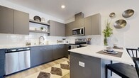 This thoughtfully designed single-floor unit accommodates three bedrooms and one bathroom within a compact, efficiently arranged floor plan. The modern kitchen serves as a visual centerpiece, featuring flat-front cabinetry in a two-tone gray palette, stainless steel appliances, a white subway tile backsplash, light quartz countertops, and a peninsula that provides additional prep and seating space. Light hardwood-style flooring runs throughout the kitchen and living areas, adding warmth to the contemporary aesthetic.

The living room offers a comfortable, well-proportioned space with a ceiling fan, light wood-tone flooring, and direct access to a private outdoor patio — ideal for bringing in natural light and fresh air. The patio itself is a sun-drenched nook suited for relaxed outdoor use.

The primary bedroom includes a dedicated walk-in closet with multi-tier shelving and hanging rods, offering notable storage capacity. Bedrooms feature windows with blinds that allow for controlled natural light. The shared bathroom is finished with a blue-gray vanity, quartz countertop, a tub-shower combination, and wood-look tile flooring, maintaining the unit's cohesive modern design language throughout.