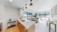 This thoughtfully designed single-floor residence offers three bedrooms and three bathrooms within a contemporary open-concept layout. Light wood flooring flows throughout, complementing the clean white walls and modern finishes that define the space.

The living and kitchen area serve as the heart of the home, where large floor-to-ceiling windows flood the space with abundant natural light and frame sweeping urban views. The kitchen features warm wood cabinetry, white quartz countertops, stainless steel appliances, a central island with seating, and stylish globe pendant lights. The living area is generously proportioned and connects seamlessly to the kitchen, creating an ideal space for entertaining.

The primary bedroom is a comfortable retreat with large windows offering city views and access to a private balcony. Each bedroom benefits from natural light and proximity to one of the three well-appointed bathrooms, which feature marble-effect tile flooring, wood vanities with white quartz countertops, LED-backlit mirrors, and glass-enclosed showers or tub-shower combinations.

A dedicated walk-in closet with built-in shelving and hanging rods provides ample storage. The hallway connecting the bedrooms is bright and efficiently laid out, with recessed lighting overhead. Overall, the space presents a clean, modern aesthetic with high-quality finishes throughout.