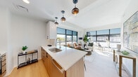 This thoughtfully designed single-floor residence offers three bedrooms and three bathrooms within a contemporary open-concept layout. Light wood flooring flows throughout, complementing the clean white walls and modern finishes that define the space.

The living and kitchen area serve as the heart of the home, where large floor-to-ceiling windows flood the space with abundant natural light and frame sweeping urban views. The kitchen features warm wood cabinetry, white quartz countertops, stainless steel appliances, a central island with seating, and stylish globe pendant lights. The living area is generously proportioned and connects seamlessly to the kitchen, creating an ideal space for entertaining.

The primary bedroom is a comfortable retreat with large windows offering city views and access to a private balcony. Each bedroom benefits from natural light and proximity to one of the three well-appointed bathrooms, which feature marble-effect tile flooring, wood vanities with white quartz countertops, LED-backlit mirrors, and glass-enclosed showers or tub-shower combinations.

A dedicated walk-in closet with built-in shelving and hanging rods provides ample storage. The hallway connecting the bedrooms is bright and efficiently laid out, with recessed lighting overhead. Overall, the space presents a clean, modern aesthetic with high-quality finishes throughout.