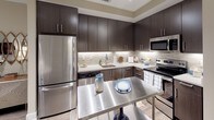 This thoughtfully designed single-floor residence offers a cohesive blend of modern style and functional living. The kitchen is a standout feature, outfitted with rich dark cabinetry, light quartz countertops, a classic subway tile backsplash, and a full suite of stainless steel appliances including a refrigerator, range, microwave, and dishwasher. The layout provides ample storage and prep space, creating an efficient and attractive cooking environment.

The open living area is warm and inviting, finished with neutral wall tones and hard-surface flooring that flows throughout the main living spaces. Large windows and a glass door lead to a private balcony, allowing natural light to fill the room and offering views of the surrounding exterior. The living room provides generous space for entertaining or relaxing.

The bedroom is carpeted for comfort, with soft neutral walls and windows dressed with blinds and curtains. A walk-in closet provides substantial storage, and direct access to the bathroom adds everyday convenience. The bathroom features a full soaking tub and shower combination with clean white tile surrounds, a vanity with dark cabinetry, and refined chrome fixtures throughout.

Overall, the space presents a polished, contemporary aesthetic with a warm and livable ambiance.