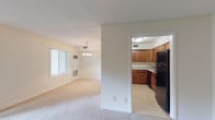 This single-floor residence offers a functional and comfortable layout designed to maximize livability. The open living area is generously sized, featuring neutral-toned carpet, soft natural light from a large sliding glass door that provides outdoor views of lush greenery, and a front entryway with additional windows fitted with blinds. A pendant chandelier illuminates the adjoining dining area, which connects seamlessly to the kitchen.

The kitchen is well-appointed with warm-toned wood cabinetry, light marble-patterned countertops, tile flooring, and black appliances including a refrigerator, dishwasher, and additional cabinetry providing ample storage space.

The bedrooms are carpeted and bathed in natural light from windows overlooking greenery outside. Each bedroom includes closet space, with some featuring sliding or paneled closet doors with built-in rods for organized storage. The primary bedroom benefits from an en-suite bathroom access.

The bathrooms are clean and functional, featuring white tile surrounds with a tub-shower combination and tile flooring. A second bathroom offers a vanity with storage. Throughout the space, the neutral color palette of whites and warm beiges creates a bright, cohesive atmosphere that is both inviting and easy to personalize.