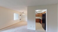 This single-floor residence offers a functional and comfortable layout designed to maximize livability. The open living area is generously sized, featuring neutral-toned carpet, soft natural light from a large sliding glass door that provides outdoor views of lush greenery, and a front entryway with additional windows fitted with blinds. A pendant chandelier illuminates the adjoining dining area, which connects seamlessly to the kitchen.

The kitchen is well-appointed with warm-toned wood cabinetry, light marble-patterned countertops, tile flooring, and black appliances including a refrigerator, dishwasher, and additional cabinetry providing ample storage space.

The bedrooms are carpeted and bathed in natural light from windows overlooking greenery outside. Each bedroom includes closet space, with some featuring sliding or paneled closet doors with built-in rods for organized storage. The primary bedroom benefits from an en-suite bathroom access.

The bathrooms are clean and functional, featuring white tile surrounds with a tub-shower combination and tile flooring. A second bathroom offers a vanity with storage. Throughout the space, the neutral color palette of whites and warm beiges creates a bright, cohesive atmosphere that is both inviting and easy to personalize.