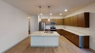 Located at 275 Huger St in Charleston, SC, this single-story unit showcases a cohesive modern design highlighted by light wood-tone flooring that flows throughout the main living areas. The open-concept kitchen serves as a centerpiece of the space, featuring warm wood-grain cabinetry extending to the ceiling, expansive granite countertops, and a sizeable island with an undermount sink and pendant lighting overhead. Stainless steel appliances, including a refrigerator, range, and built-in microwave, complete the well-equipped kitchen.

The bedrooms are generously proportioned, with ceiling fans, recessed lighting, and natural light provided through windows fitted with white plantation blinds. One bedroom features soft carpeting, while others continue the wood-look flooring theme. A spacious walk-in closet with wire shelving systems offers practical storage solutions.

The bathrooms reflect the same refined aesthetic, featuring wood-tone vanities, granite countertops, and large mirrors. One bathroom includes a glass-enclosed walk-in shower with marble-style tile surround, while another offers a combination tub and shower. Both bathrooms benefit from natural light through slatted blinds. The overall ambiance throughout the unit is clean, contemporary, and well-finished.