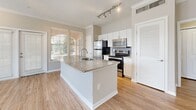 This 730-square-foot, one-bedroom, two-bathroom unit at 2054 Riverside Avenue in Jacksonville, FL offers a well-designed single-floor layout with cohesive finishes throughout. The open-concept kitchen and living area serves as the heart of the home, featuring a large granite countertop island with an undermount sink, white shaker cabinetry, stainless steel appliances including a refrigerator, electric range, and microwave, plus a subway tile backsplash and track lighting overhead. Crown molding and wood-style flooring flow seamlessly into the bright living room, which is lined with multiple windows fitted with blinds, allowing ample natural light, and is finished with a ceiling fan. The 160-square-foot primary bedroom provides a comfortable retreat with its own ceiling fan, neutral tones, and access to a dedicated walk-in closet with built-in shelving. A hallway connects the two bathrooms, one of which features a granite-topped vanity with white cabinetry, while the other includes a full tub-shower combination with tile surround and wood-style flooring. Clean white trim, panel-style doors, and a neutral color palette unify the space, creating a bright and functional living environment.