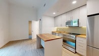 Located at 29 Crown Street in New Haven, CT, this efficiently designed one-bedroom, one-bathroom unit offers a thoughtfully planned layout across a single floor. The open-concept kitchen and living area serves as the heart of the unit, featuring light hardwood flooring, recessed lighting, and soaring ceilings that amplify the sense of space. The kitchen is well-appointed with sleek white cabinetry extending to the ceiling, warm butcher block countertops, stainless steel appliances including a gas range and full-size refrigerator, and a central island that doubles as a prep and dining surface. The bedroom is carpeted for comfort and features wood-trimmed windows that invite natural light and outdoor views of the surrounding area. A striking natural wood accent wall adds warmth and texture to the room. The dedicated closet space offers built-in floor-to-ceiling white cabinetry with integrated drawers, providing ample and organized storage. The bathroom is finished in a clean, modern style with white tile surround, a soaking tub with shower, wood-look flooring, and a white vanity with a broad countertop. Throughout the unit, the design maintains a cohesive, contemporary aesthetic with a neutral palette and quality finishes.