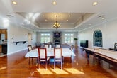 Located at 333 Lancaster Avenue in Malvern, PA, this well-appointed single-floor space offers a generous, open layout designed for both gathering and relaxation. Rich, polished hardwood floors run throughout, reflecting natural light that pours in from multiple large windows and offering a warm, inviting ambiance.

The main gathering area is anchored by a dramatic floor-to-ceiling stacked stone fireplace with a mounted flat-screen television above — a striking focal point that defines the lounge seating area. An elegant tray ceiling with a classic chandelier and recessed lighting adds architectural depth above the dining area, which comfortably accommodates a large table and chairs.

A dedicated billiards area with a full-size pool table and wall-mounted cue rack provides a recreational element, while an open arched mirror accent wall adds a refined decorative touch. French doors with glass panes lead to additional areas, enhancing the sense of openness and connectivity throughout the space.

The kitchen features wood cabinetry, granite countertops, and a full-size refrigerator. Two bathrooms and a welcoming entrance complete the layout. Crown molding, neutral gray walls, and abundant natural views of the surrounding greenery contribute to a polished yet comfortable atmosphere throughout.