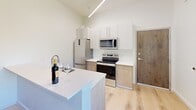 Located at 440 Monroe Ave in Memphis, TN, this modern two-story unit offers a well-organized layout designed to maximize every square foot across two floors. The main level houses the kitchen and living area, where light hardwood flooring and crisp white walls create a clean, contemporary aesthetic. The kitchen is a standout feature, equipped with stainless steel appliances — including a refrigerator, electric range, and microwave — paired with two-tone cabinetry in white and warm wood tones, white quartz countertops, and a peninsula that doubles as a breakfast bar. Soaring ceilings with linear pendant lighting add an airy, loft-like feel to the space.

The upper floor is home to the generously sized bedroom, which benefits from a large window and a glass-paned door opening to a private balcony with outdoor views. A ceiling fan and additional linear lighting keep the room comfortable and well-lit. The continuity of light hardwood flooring flows throughout both levels, tying the space together seamlessly.

The full bathroom features warm hardwood floors, white subway tile surrounding the shower-tub combo, and clean white fixtures, maintaining the home's cohesive modern style. A hallway connects the rooms efficiently, completing this thoughtfully designed urban residence.