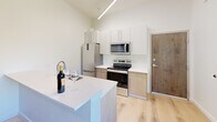 Located at 440 Monroe Ave in Memphis, TN, this modern two-story unit offers a well-organized layout designed to maximize every square foot across two floors. The main level houses the kitchen and living area, where light hardwood flooring and crisp white walls create a clean, contemporary aesthetic. The kitchen is a standout feature, equipped with stainless steel appliances — including a refrigerator, electric range, and microwave — paired with two-tone cabinetry in white and warm wood tones, white quartz countertops, and a peninsula that doubles as a breakfast bar. Soaring ceilings with linear pendant lighting add an airy, loft-like feel to the space.

The upper floor is home to the generously sized bedroom, which benefits from a large window and a glass-paned door opening to a private balcony with outdoor views. A ceiling fan and additional linear lighting keep the room comfortable and well-lit. The continuity of light hardwood flooring flows throughout both levels, tying the space together seamlessly.

The full bathroom features warm hardwood floors, white subway tile surrounding the shower-tub combo, and clean white fixtures, maintaining the home's cohesive modern style. A hallway connects the rooms efficiently, completing this thoughtfully designed urban residence.
