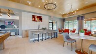 The Lounge & Game Room at Canopy Apartment Villas in Pelham, Alabama, is a thoughtfully designed single-level amenity space that seamlessly blends relaxation and entertainment. The open-concept layout is anchored by soaring ceilings clad in warm natural wood paneling, complemented by large-format light tile flooring that extends throughout the entire space. Dramatic wrought-iron ring chandeliers and recessed lighting provide layered illumination, enhancing the contemporary yet inviting atmosphere.

The game area is centered around a substantial rustic wood-framed pool table, accompanied by a wall-mounted flat-screen TV and a bar-height counter with sleek stools—ideal for casual socializing. Adjacent to the game zone, a white tile-accented wet bar features warm wood cabinetry, a matte black faucet, and an overhead TV display, offering a functional gathering point.

The lounge area provides two distinct seating zones: one featuring plush gray sofas, textured area rugs, and a wall-mounted TV framed by large artwork, and another with tufted cognac leather chairs arranged to face floor-to-ceiling windows. These expansive windows flood the space with natural light and offer direct views of the outdoor pool area, creating a seamless indoor-outdoor connection that defines the overall ambiance of this vibrant community gathering space.