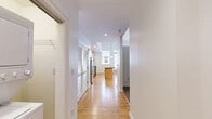 Located at 230 N 6th St in downtown Richmond, VA, this efficiently designed unit on the second floor offers a well-appointed single-floor layout. The open-concept kitchen serves as the centerpiece of the space, showcasing light maple cabinetry, dark granite countertops, a subway tile backsplash, and a full suite of stainless steel appliances including a refrigerator, electric range, and built-in microwave. A kitchen island with a matching dark countertop provides additional prep space and separates the kitchen from the living area. Globe pendant lights hang above, adding a modern touch. Warm-toned hardwood floors extend throughout the main living areas, contributing to a cohesive and inviting atmosphere. The living area benefits from natural light streaming through a set of French doors with transom windows above, lending an airy, open feel. The bathroom features a granite-topped vanity with maple cabinetry, a large mirror, and elegant crystal-style sconce lighting, complemented by tile flooring. A convenient in-unit laundry closet with a stacked washer and dryer is accessible just off the bathroom, adding a practical amenity. The unit's location within a classic multi-story building reflects Richmond's architectural character.