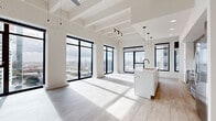 Located in the heart of Houston at 1801 Smith St, this thoughtfully designed 2-bedroom, 2-bathroom residence offers a refined urban living experience. The open-concept living and kitchen area is an immediate showstopper, boasting soaring exposed-beam ceilings, light hardwood flooring, and dramatic floor-to-ceiling black-framed windows that flood the space with natural light and frame sweeping views of the Houston skyline. The gourmet kitchen features a large waterfall-edge island with an undermount sink, sleek white cabinetry paired with warm wood-toned upper cabinets, stainless steel appliances, and modern cylindrical pendant lighting. A light-filled hallway with recessed lighting and paneled white doors connects the living areas to the private quarters. Both bedrooms are carpeted and generously proportioned, with the primary bedroom offering notable square footage, large black-framed windows with city views, and access to a well-appointed closet with built-in shelving and chrome hanging rods. The bathrooms are elegantly finished, featuring wood-toned vanities, matte black fixtures, illuminated mirrors, and marble-tiled tub-shower combinations. This residence combines contemporary design with an abundance of natural light and striking urban vistas.
