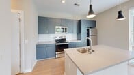 Located at 906 Waterfront Dr in Knoxville, Tennessee, this single-floor residence offers a well-designed, contemporary living experience. The open-concept living area features light wood-look flooring, recessed lighting, and large sliding glass doors that lead to a private balcony, allowing abundant natural light and offering pleasant outdoor views of the surrounding landscape and waterfront area. The kitchen is a standout feature, outfitted with bold slate-blue cabinetry extending to the ceiling, a white subway tile backsplash, light quartz countertops, a central island with an undermount sink, and a full suite of stainless steel appliances including a refrigerator, electric range, and built-in microwave. The bedrooms are finished with plush neutral carpet and feature windows with blinds that frame outdoor views, providing a comfortable and quiet retreat. A spacious walk-in closet with wire shelving and hanging rods offers generous storage. The bathroom is clean and functional, featuring a glass-door walk-in shower, wood-look flooring, a vanity with countertop sink, and built-in wire shelving for additional storage. Neutral warm-toned walls throughout the space create a cohesive and inviting ambiance well-suited for modern living.