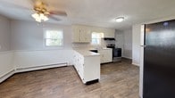 This two-floor space is finished in a neutral gray palette that lends a clean, understated character throughout. The main level features wood-look flooring that flows through the living area and into the kitchen. The living space is bright and open, with large windows admitting generous natural light and views of the surrounding neighborhood. A staircase connects the two floors, and a wall-mounted air conditioning unit provides supplemental cooling on this level.

The kitchen is well-appointed with white cabinetry, light countertops, a double stainless steel sink, and a stainless electric range. A peninsula provides additional counter space and a natural division between the kitchen and adjacent areas. A ceiling fan with a light fixture adds both function and airflow to this space.

The upper level hosts multiple carpeted bedrooms, each finished with the same soft gray walls and outfitted with baseboard heating. Bedrooms benefit from multiple windows, allowing ample natural light. One bedroom includes a wall-mounted air conditioning unit for independent climate control. Closet space is provided with full-width reach-in closets featuring hanging rods.

The bathroom includes a tub-shower combination, a window for natural light and ventilation, and consistent wood-look flooring tying it to the rest of the home.