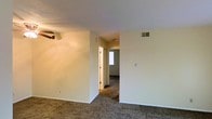 This single-story residence offers a straightforward and functional layout designed for comfortable everyday living. The interior features wall-to-wall carpeting throughout the main living areas, providing a warm and soft underfoot feel. Neutral, light-toned walls create a clean and versatile backdrop, making the space easy to personalize and furnish to taste.

A central hallway connects the living area to the adjacent rooms, promoting an efficient flow throughout the home. Visible HVAC vents integrated into the ceiling indicate a central air system, ensuring year-round climate comfort. A ceiling fan is present in the main living area, adding both practical ventilation and a subtle design element to the room.

Natural light filters in through a window visible at the end of the hallway, brightening the interior and contributing to an open, airy feel despite the compact scale of the space. The doors are finished in a classic style, complementing the clean lines of the overall interior. White baseboards trim the perimeter of each room, adding a crisp, finished look to the carpeted floors.

Overall, this single-floor home presents a no-frills, move-in ready environment with a sensible layout, consistent finishes, and essential amenities that make it a practical and comfortable place to call home.