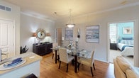 This single-story residence in Conroe, Texas offers a well-organized layout with a cohesive coastal-inspired color palette featuring soft aqua accents, warm neutral walls, and wood-look flooring throughout the main living areas. The living room is bright and welcoming, with large sliding glass doors framed by floor-to-ceiling drapes that invite natural light and provide access to an outdoor patio. Crown molding and a ceiling fan add refined detail to the space.

The kitchen is equipped with rich espresso-toned cabinetry, black appliances including a range, microwave, and refrigerator, and a central island with a light countertop ideal for casual dining. It flows seamlessly into a dedicated dining area, which features hardwood-style flooring, crown molding, and an elegant pendant light fixture above a glass-top dining table.

The bedrooms feature plush carpeting, ceiling fans, and ample natural light from multiple windows. One bedroom includes vaulted ceilings and direct access to a full bathroom. A walk-in closet with wire shelving connects conveniently to a secondary bathroom with a tub-shower combination and wood-look flooring. A dedicated laundry area houses a full-size side-by-side washer and dryer, adding everyday practicality to this thoughtfully designed home.