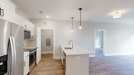 Located at 1425 Aversboro Rd in Garner, NC, this single-floor home offers a clean, modern aesthetic throughout. The open-concept kitchen is a standout feature, showcasing white shaker-style cabinetry with matte black hardware, stainless steel appliances including a French door refrigerator and range, and a center island with a white quartz countertop, undermount sink, and stylish pendant lighting overhead. Light wood-tone luxury vinyl plank flooring flows seamlessly throughout the home, providing both durability and visual continuity. The living area is bright and airy, featuring a ceiling fan and a large picture window with transom detail that frames views of surrounding trees. A glass door opens directly to a private outdoor deck with black metal railing, extending the living space outdoors. Bedrooms are well-proportioned, each finished with LVP flooring, ceiling fans, and generous windows that invite natural light and wooded views. A walk-in closet with wire shelving systems provides ample organized storage. The bathroom includes a soaking tub, toilet, and grab bars, finished in a clean, neutral palette. A dedicated laundry room houses a full-size Whirlpool washer and dryer with overhead wire shelving. The home's consistent use of neutral tones, modern fixtures, and quality finishes creates a cohesive and inviting living environment.
