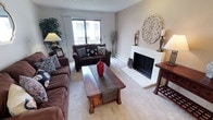 Located at 702 W Casino Rd, Unit 204 in Everett, Washington, this single-floor residence offers a well-organized layout with comfortable living spaces throughout. The living room serves as the centerpiece of the home, featuring a classic white brick fireplace, plush carpeting, and a sliding window that draws in natural light and outdoor views. The space is generously sized to accommodate multiple seating arrangements, creating a warm and inviting atmosphere. Adjacent to the living room, the dining area is highlighted by a chandelier overhead and a pass-through counter that connects directly to the kitchen, promoting an open flow between spaces. The galley-style kitchen is efficiently designed with dark cabinetry, light countertops, tile flooring, and a full suite of appliances including a range, dishwasher, and refrigerator. The residence includes two bedrooms, both carpeted and featuring windows that allow natural light to filter in. The primary bedroom offers ample space, while the second bedroom provides a comfortable and functional retreat. A full bathroom completes the layout, featuring a tub-shower combination, tile flooring, and a vanity with stone-style countertops. Textured ceilings and baseboard heating are consistent features throughout the home.