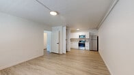 Located at 415 W Franklin St in downtown Tucson, this single-floor unit features a clean, modern design with a cohesive neutral color palette and light wood-tone flooring carried throughout every room. The open living and kitchen area provides a functional, airy feel, with the kitchen outfitted in crisp white cabinetry, a neutral tile backsplash, and a full suite of stainless steel appliances including a range, microwave, refrigerator, and dishwasher. A dedicated in-unit laundry area with a stacked washer and dryer is conveniently tucked adjacent to the kitchen, adding practical value to the layout. Multiple rooms offer wall-mounted HVAC units for individual climate control, and several spaces feature windows with blinds that allow natural light to filter in while maintaining privacy. One room includes a ceiling fan with a light fixture, enhancing comfort and airflow. The bathroom is neatly appointed with a tub-shower combination, a white vanity with a light stone-style countertop, and wood-look tile flooring that complements the rest of the unit. Throughout, the white walls and minimalist finishes create a bright, clean atmosphere well-suited to a variety of living arrangements.