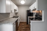 This two-floor residence offers a practical and well-maintained layout with modern finishes throughout. The main level features a welcoming living area with rich wood-look hardwood-style flooring, neutral painted walls, and a staircase with black metal railing leading to the upper floor. A wall-mounted AC unit and a front entry door with an adjacent window allow natural light to fill the space.

The galley-style kitchen is thoughtfully designed with white shaker cabinetry, granite-look countertops, a stainless steel sink, and dark hardwood-style flooring. Appliances include a black electric range with overhead ventilation, a stainless steel dishwasher, and a full-size refrigerator, all set beneath a flush ceiling light fixture.

The bathroom is clean and functional, featuring tile flooring in a herringbone pattern, a full soaking tub and shower combo, a white vanity with granite-style countertop, and bright white finishes throughout.

The upper-level bedrooms are carpeted and feature ceiling fans with light fixtures, and windows with blinds that bring in natural light. The rooms offer a quiet, comfortable atmosphere with neutral tones and clean lines. Overall, the space presents a move-in-ready environment with consistent, updated finishes across both floors.