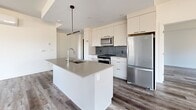 Located at 487 Broad St in Halifax, Nova Scotia, this modern 2-bedroom, 2-bathroom unit offers a thoughtfully designed single-floor layout with generous living space throughout. The open-concept kitchen and living area serves as the heart of the home, featuring a sleek central island with an undermount sink, quartz-style countertops, white cabinetry extending to the ceiling, a grey mosaic tile backsplash, and a full suite of stainless steel appliances including a refrigerator, range, and microwave. A contemporary pendant light fixture adds a stylish focal point above the island. The spacious living room is bathed in natural light through multiple large windows overlooking lush greenery, with durable hardwood-style flooring running throughout. Both bedrooms are well-proportioned and bright, with the primary bedroom featuring a generous walk-in closet outfitted with built-in shelving and hanging rods. A second closet provides additional storage. The two bathrooms are finished in a clean, modern palette, with one featuring a soaker tub and tiled surround, a white vanity with dark hardware, and large-format floor tiles. A connecting hallway ties the layout together efficiently, completing this well-appointed Halifax residence.