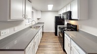 Located at 564 E Barham Dr in San Marcos, California, this single-story residence offers a thoughtfully designed layout with a clean, modern aesthetic throughout. The open living area features rich, dark wood-style flooring and a sliding glass door fitted with vertical blinds, allowing natural light to fill the space while providing access to the outdoors. The galley-style kitchen is well-appointed with white cabinetry, gray countertops, a stainless steel sink, and black appliances including a refrigerator, electric range, and built-in microwave, all set atop durable wood-look flooring. The bedrooms are carpeted for comfort and feature neutral toned walls, blinds-covered windows that bring in natural light, and generous closet space, including a sliding-door closet in the primary bedroom. The bathrooms are finished with wood-style flooring, white cabinetry, gray countertops, and modern fixtures. One bathroom features a full tub-shower combination, while another includes a spacious vanity with a wide mirror and contemporary lighting. The consistent use of neutral tones, clean lines, and updated finishes creates a cohesive and practical living environment throughout the home.