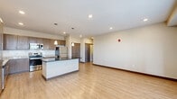 This well-appointed one-bedroom, one-bathroom residence in Plainfield, Indiana offers a thoughtfully designed single-floor layout with a cohesive blend of modern finishes and functional living spaces. The open-concept kitchen and living area serves as the heart of the home, showcasing light wood-tone flooring, recessed lighting, and a central kitchen island with a dark countertop. The kitchen is fully equipped with stainless steel appliances—including a refrigerator, range, microwave, and dishwasher—complemented by rich medium-toned cabinetry, a classic subway tile backsplash, and granite-style countertops. Pendant lights above the island add a stylish touch. The living area is bright and open, featuring a glass-panel exterior door and multiple windows that invite natural light. The spacious primary bedroom is finished with plush carpeting, a ceiling fan with light fixture, and multiple windows offering ample natural light. The full bathroom features a walk-in shower with grab bars, a vanity with granite-style countertop, and wood-look tile flooring. A dedicated laundry closet houses full-size washer and dryer units. A hallway with closet storage completes this efficiently designed and move-in-ready residence.
